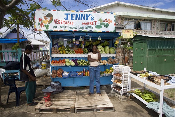 WEST INDIES, St Vincent & The Grenadines, Union Island, Fruit and vegetable market stall with owner in Hugh Mulzac Square in Clifton