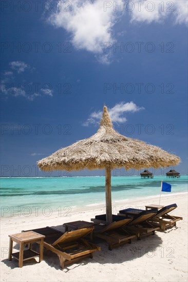 WEST INDIES, St Vincent & The Grenadines, Canouan, Palapa thatched shelter and sunbeds on Godahl Beach at Raffles Resort with offshore treatment rooms of the Amrita Spa beyond