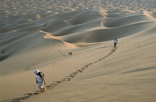 MOROCCO, Sahara, Merzouga, Tourists walking through desert landscape leaving trails of footprints across the dunes.