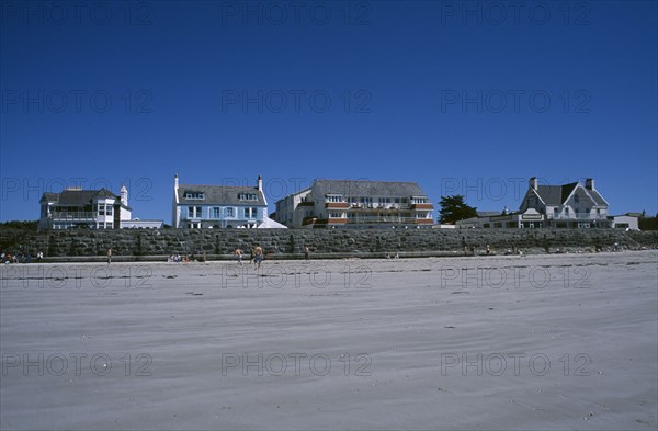 UNITED KINGDOM, Channel Islands, Guernsey, Castel. Cobo Bay. View across sandy beach with sunbathers and people playing football towards hotels and restaurants
