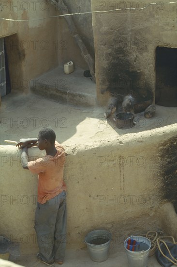 BURKINA  FASO, Sapone, Young man standing against wall in traditional Gurunsi village.