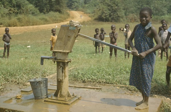 GHANA, Children, Young girl using village hand pump near Euchi.