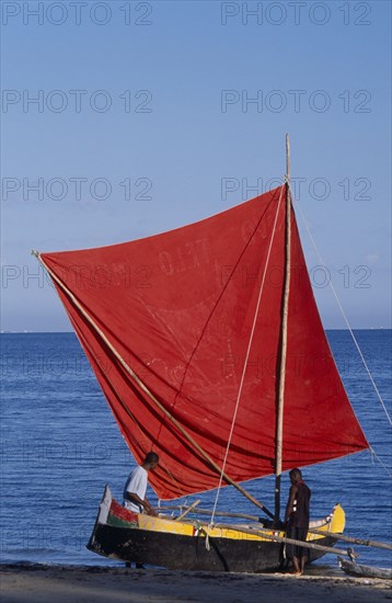 MADAGASCAR, Tulear, Ifaty Beach. Men with a red sail Pirogue boat at the waters edge