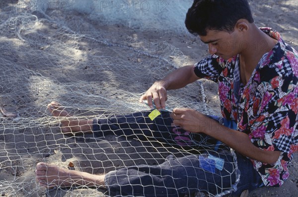 DOMINICAN REPUBLIC, Beach, Fisherman mending net on beach.