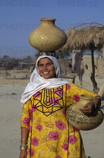 PAKISTAN, Sindh Province, Gurmani, "Woman collecting water, carrying one pot on her head and another under her arm."