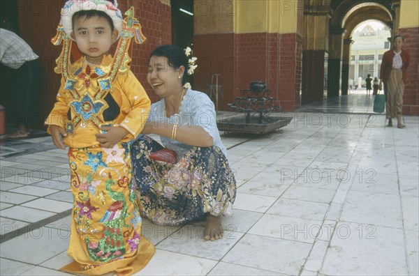 MYANMAR, Mandalay, Young boy being dressed by woman for ordination ceremony Mahamuni Paya. Great sage Pagoda.