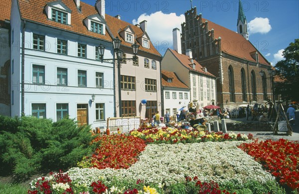 LATVIA, Riga, Church of St John beside town housing with colourful flowerbeds in the foreground on Skunu Street.