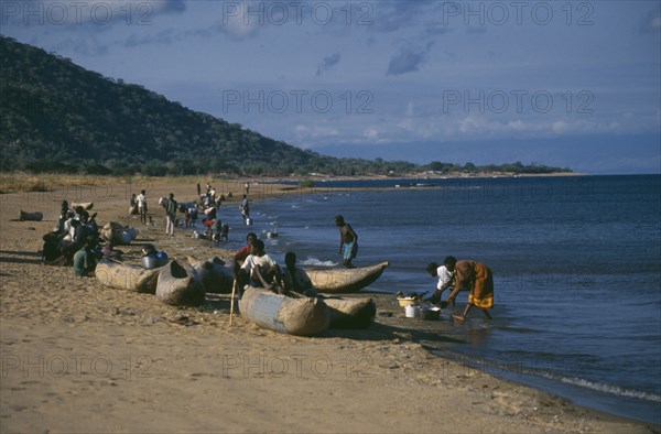 MALAWI, Lake Malawi, Cape Maclear with children playing on shore in wooden canoes and women washing dishes.