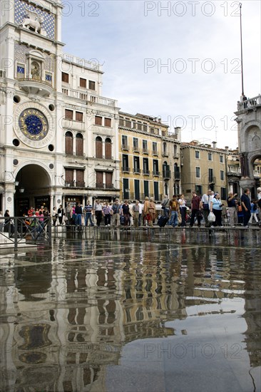 ITALY, Veneto, Venice, Aqua Alta High Water flooding in St Marks Square with tourists on elevated walkways above the flooded piazza beside St Marks Basilica and the Torre dell'Orologio clock tower