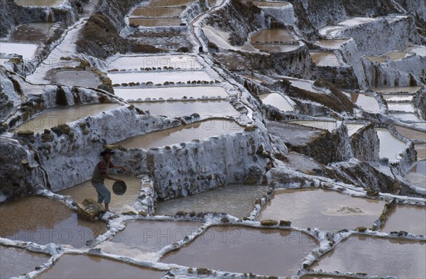 PERU, Cusco, Salinas, Man working on salt terraces near Maras used to collect salt by evaporation since Inca times.