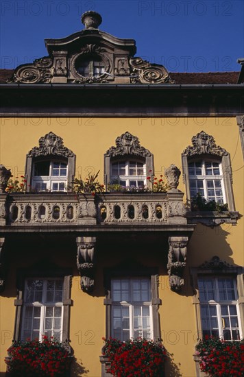 HUNGARY, Budapest, Detail of yellow painted facade of town building with stone balconies and window boxes filled with red geraniums and other flowers. Eastern Europe