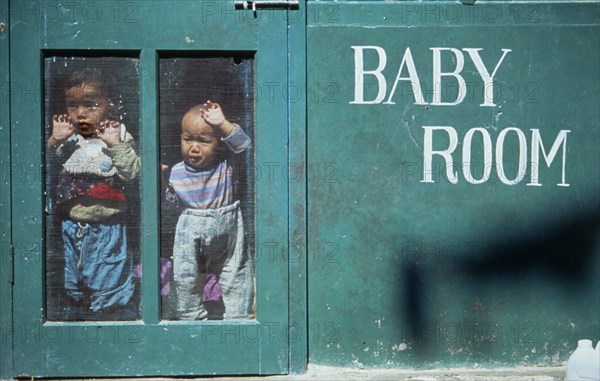 INDIA, Himachal Pradesh, Dharamsala, Young Tibetan refugee children looking out from inside creche.