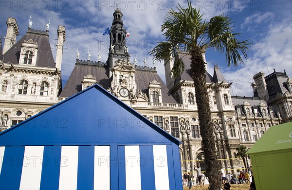 FRANCE, Ile de France, Paris, The Paris Plage urban beach. Young people playing beach volleyball behind beach huts in front of the Hotel de Ville Town Hall