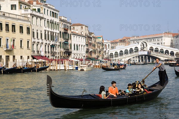 ITALY, Veneto, Venice, Sightseeing tourists in a Gondola on the Grand Canal with the Rialto Bridge behind them