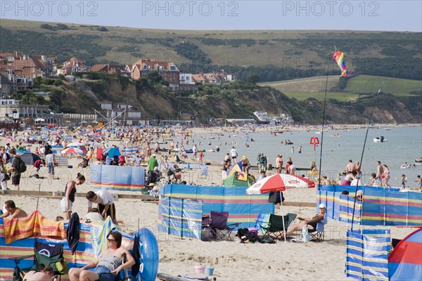 ENGLAND, Dorset, Swanage Bay, Sunbathers on busy sandy beach with colourful windbreaks and inflatables overlooked by hotels