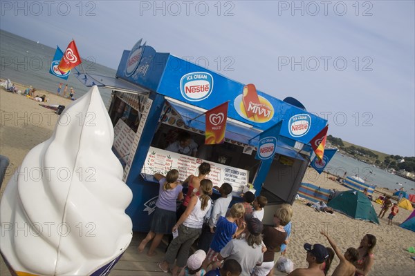 ENGLAND, Dorset, Swanage Bay, A group of children queuing at an Ice Cream stall. Angled view with a large plastic ice cream in the foreground.