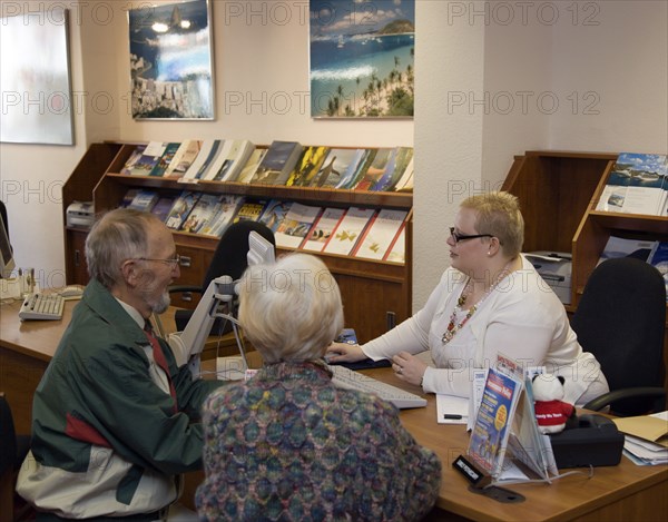 ENGLAND, West Sussex, Chichester, Male and female customer in a Travel Agents office discussing their holiday arrangements with a female travel consultant