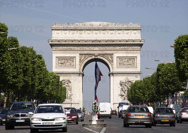 FRANCE, Ile de France, Paris, Traffic in the Champs Elysees leading to the Arc de Triomphe in Place de Charles de Gaulle with the French tricolour hanging from the central arc