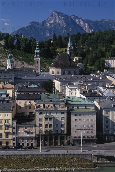 AUSTRIA, Salzburg, City view with Untersburg Mountain behind.  Church spire and towers and buildings with flat rooftops and roof and window balconies.