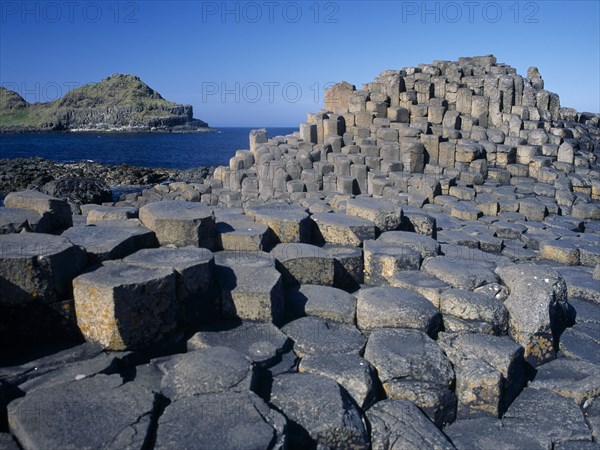 NORTHERN IRELAND, County Antrim, Giants Causeway, Interlocking basalt stone columns left by volcanic eruptions. View across the stones towards cliffs and coastline