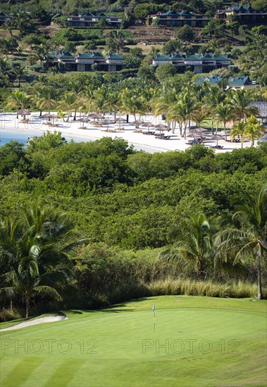WEST INDIES, St Vincent & The Grenadines, Canouan, "Raffles Resort Trump International Golf Course designed by Jim Fazio. The 8th green with the resort and Jambu beach beyond lined with coconut palm trees, palapas and sunbeds"
