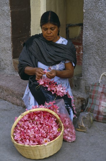 MEXICO, Guerrero, Woman flower seller sitting on step in street threading pink flower heads into garland.