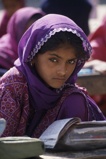 INDIA, Rajasthan, Jhunjhunu, A young girl student dressed in purple sitting at a desk with books at the mosque school in the Dargah Hazrat Qamruddin Shah Sahib