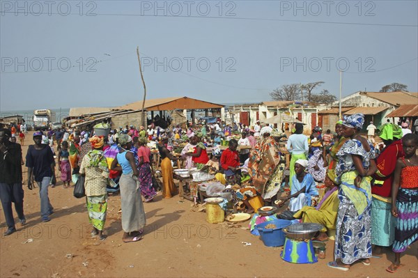 GAMBIA, Western Gambia , Tanji, Tanji market.  Busy market scene with line of food stalls and crowds of people in brightly coloured dress.