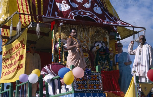 ENGLAND, East Sussex, Brighton, Hare Krishna taking part in a parade on Brighton seafront  with a colourful painted carriage