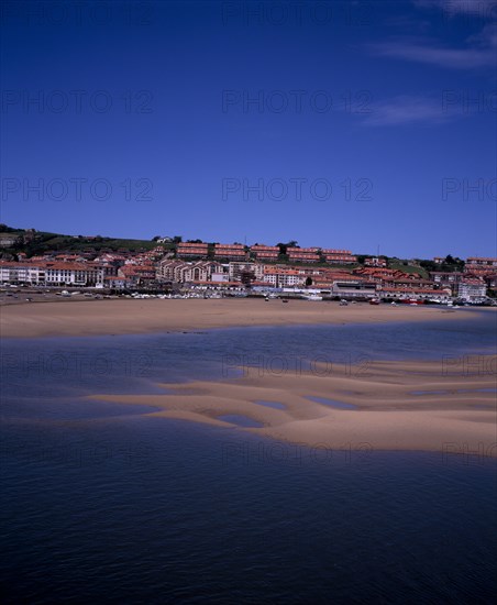 SPAIN, Cantabria, San Vicente de la Barquera, Town buildings extending to sea wall with moored boats on sand bars at low tide on the Rio del Escudo estuary.
