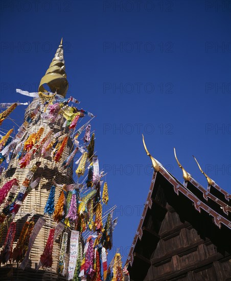 THAILAND, North, Chiang Mai, Wat Phran Tao.  Detail of pointed roof top of rare teak temple beside woven tower decorated by children with coloured paper flags and offerings.