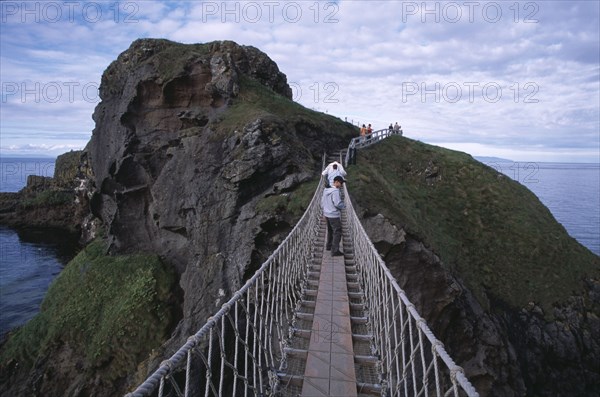 NORTHERN IRELAND, County Antrim, Ballintoy, Carrick-a-Rede Rope Bridge. Vistors walking over rope bridge linking a rocky island to cliffs.