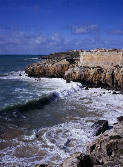 PORTUGAL, Estremadura, Ribatejo, Peniche. Atlantic Ocean town. Sea and cliffs topped by part of curtain wall to the 16th Century Fortaleza Castle situated south of the town.