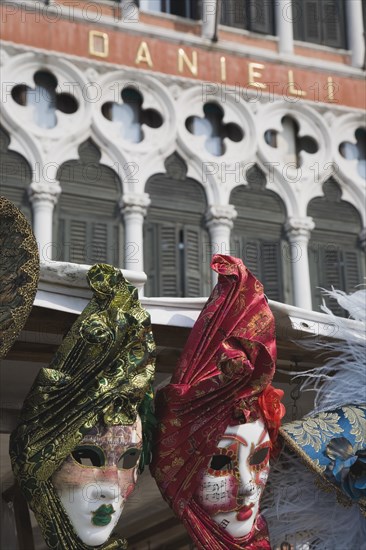 Venice, Veneto, Italy. Red green blue and gold carnival masks in front of partly seen facade of the Hotel Danieli. Italy Italia Italian Venice Veneto Venezia Europe European City Masks Mask Festival Carnival Architecture Facade Facade Hotel Color Destination Destinations Southern Europe