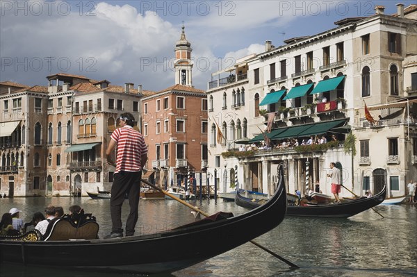 Venice, Veneto, Italy. Gondolier manoeuvres gondola before start of Regata Storico the Venice annual historical Regatta in September. Canalside buildings behind. Italy Italia Italian Venice Veneto Venezia Europe European City Regata Regatta Storico Gondola Gondolas Gondolier Boat Architecture Exterio Exterior Water Blue Clouds Cloud Sky Destination Destinations History Historic One individual Solo Lone Solitary Southern Europe