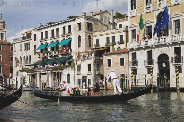 Venice, Veneto, Italy. Participants in the Regata Storico historical Regatta held annually in September wearing traditional costume approaching the Rialto bridge with onlookers gathered on balconies of canalside buildings behind. Teams represent Sestiere districts of Venice in traditional races. Italy Italia Italian Venice Veneto Venezia Europe European City Regata Regatta Gondola Gondola Gondolas Gondolier Boat Architecture Exterior Water Classic Classical Destination Destinations History Historic Holidaymakers Older Southern Europe Tourism Tourist