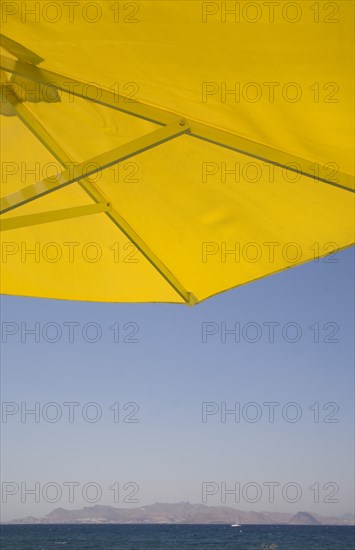 Kos, Dodecanese Islands, Greece. Underside of bright yellow sun umbrella framing view across sea to distant coastline. Greece Greek Europe European Vacation Holiday Holidays Travel Destination Tourism Ellas Hellenic Docecanese Kos Beach Sea Umbrella Parasol Yellow Blue Color Destination Destinations Ellada Sand Sandy Beaches Tourism Seaside Shore Tourist Tourists Vacation Southern Europe Water