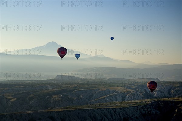 Early morning with hot air balloons in flight above tufa landscape with Mount Erciyes in the background. Photo : Hugh Rooney