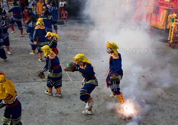 Thai boys in Chinese character costume dancing and drumming with firecrackers exploding at local temple.